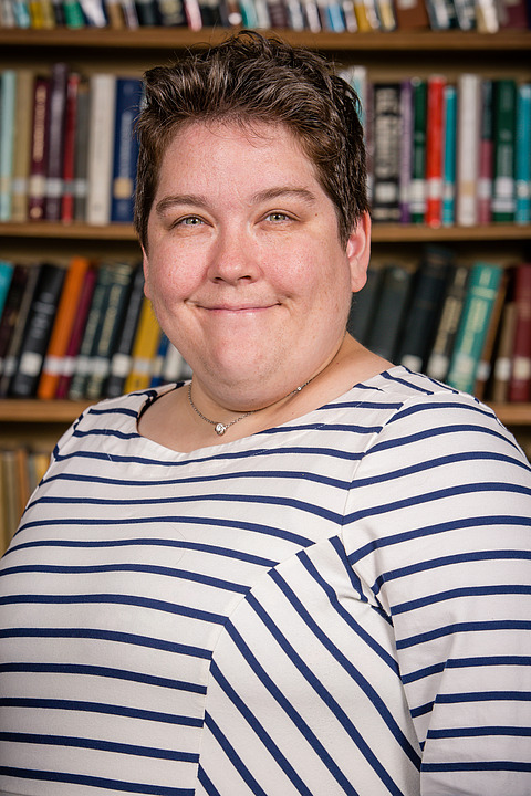 brown haired white woman in striped white dress in front of books